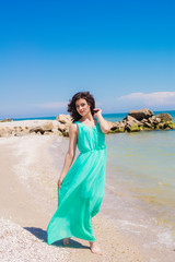 Young beautiful girl in  dress on the beach in summer. The girl in the blue sea on the sand
