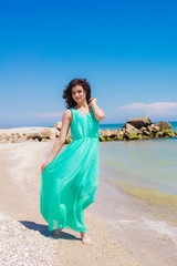 Fototapeta na wymiar Young beautiful girl in dress on the beach in summer. The girl in the blue sea on the sand