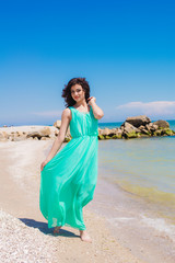 Young beautiful girl in  dress on the beach in summer. The girl in the blue sea on the sand