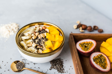 Breakfast oatmeal porridge with fresh fruits, chia seeds and hazelnut on gray background. Oatmeal with mango and banana. Healthy breakfast concept. Mockup, overhead, copy space