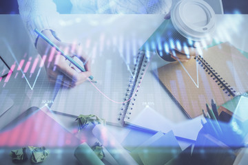Financial forex graph displayed on hands taking notes background. Concept of research. Multi exposure