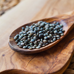 Green French lentils - puy dal on wooden spoon.