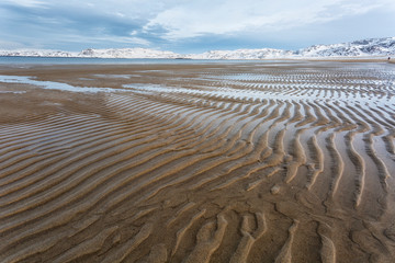 Large sandy beach on the shore of the Barents Sea with traces of water. In the background are mountains.