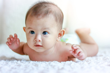 The baby boy does not wear clothes. Lying on a white bed, he looks happy