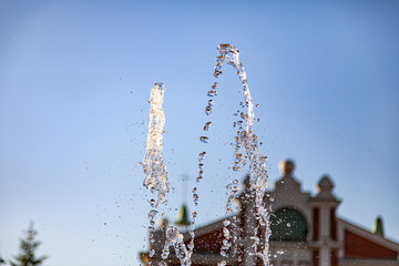 Naklejka na ściany i meble City fountain with splashes and tops jets of water frozen in the air on a clear summer day against the blue clear sky. Freshness and benefits of fluid.