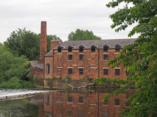 Fototapeta na wymiar thwaite mill leeds built in 1825 on an island between the river aire and calder navigation canal reflected in the water and surrounded by trees