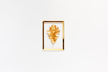 Autumn composition. Golden frame with a gold spray painted natural leaf on white background. Flat lay, top view, copy space.