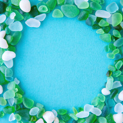 Close up of various sea glass pieces with empty circle shape in the middle on blue background. Design template. Frame with copy space for text. Top view, flat lay