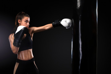 Woman boxer fighting in gloves with boxing punching bag on black background. Boxing and fitness...