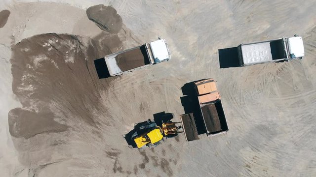 Top view of an excavator filling trucks with construction materials