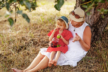 Happy grandmother with granddaughter spend a fun time hugging together in summer outdoors. Rest under a tree eat berries and apples. Family and healthy food