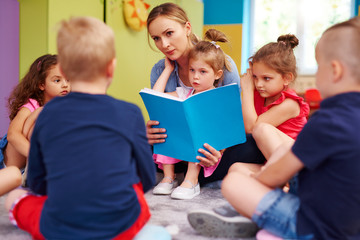 Female teacher is reading a book during classes in preschool - obrazy, fototapety, plakaty