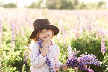 smiling girl in a hat collects a bouquet of lupins at sunset