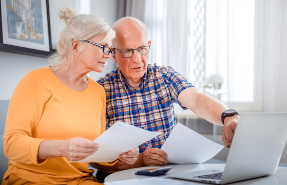 Worried senior couple checking bills using laptop at home