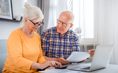Worried senior couple checking bills using laptop at home