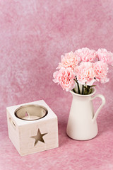 Florero con claveles rosas y vela blanca.