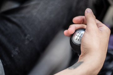 Detalle de mano de hombre con tatuaje cambiando de marchas conduciendo un coche 