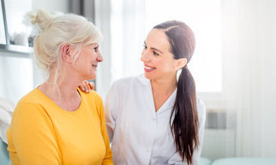 Smiling nurse talking with senior female during home visit