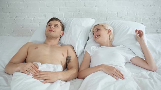 handsome man talking and kissing beautiful smiling woman in bed