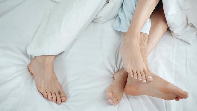 cropped view of couple lying in bed and touching legs at home