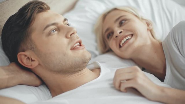 man talking and stroking beautiful laughing and smiling woman in bed