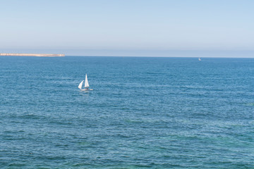 Fototapeta premium A lonely sailboat sailing on a blue calm sea on a sunny summer day