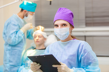 Beautiful portrait of a doctor with documents on the background of the operating room. Baldness treatment. Hair transplant. Surgeons in the operating room carry out hair transplant surgery. Surgical