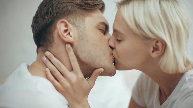 beautiful woman embracing and kissing smiling man at home