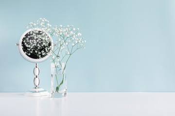 Soft light bathroom decor in pastel blue color, mirror, white flowers, accessories on white wood shelf. Elegant decor bathroom interior.