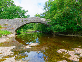Fototapeta na wymiar The River Ribble passes under an old stone bridge near Stainforth