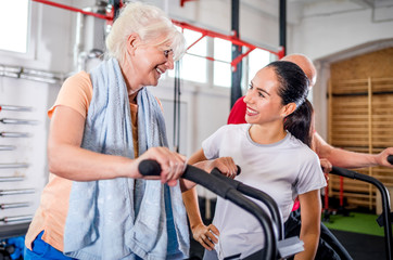 Senior woman biking at the gym with personal trainer