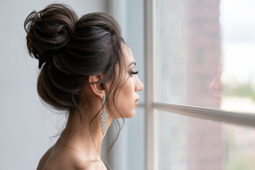 beautiful girl with hairstyle high beam looks out window. Evening image girl.