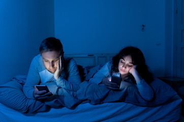 Couple in bed on smart phones ignoring each other in relationshi
