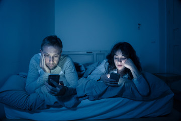 Fototapeta na wymiar Couple in bed on smart phones ignoring each other in relationshi