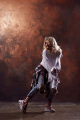 Fototapeta na wymiar Photo of young dancing blonde girl in torn jeans on brown background