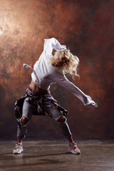 Photo of slender blonde dancer with developing hair in torn jeans and sneakers on dark brown...
