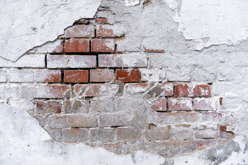 brick wall background with white fallen off plaster. The brick wall is visible from under the white...