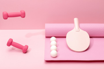 pink dumbbells levitating in air near white ping-pong balls and racket on fitness mat on pink background