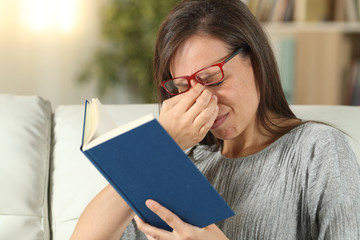 Woman with eyeglasses suffering eyestrain reading a book