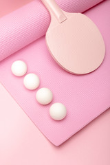 white ping-pong balls and racket on fitness mat on pink background