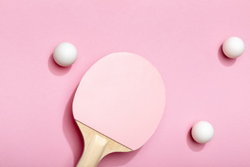 top view of white table tennis balls scattered near pink racket on pink background