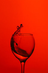 splash of water in wineglass isolated on red background.