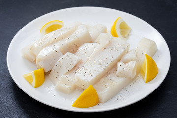 raw squid with pepper and fresh lemon on white plate