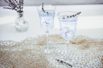 Fresh lavender lemonade with flowers and ice cubes in beautiful glasses on white wooden table. Detox water. Summer drink. Diet cocktail. Selective focus. Copy space.