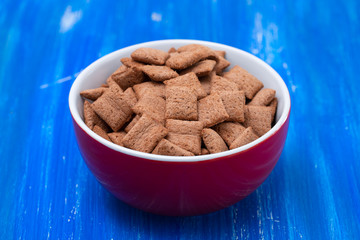 Chocolate pillows in red bowl on blue wooden background