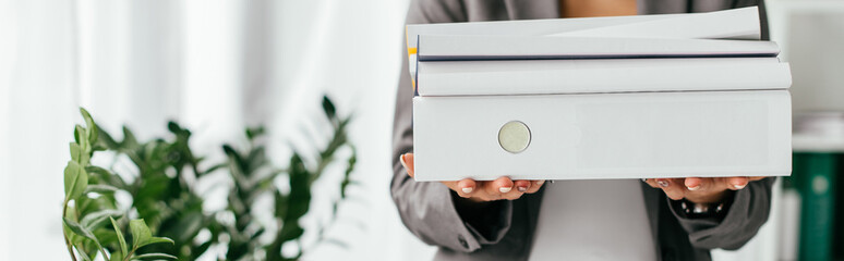 panoramic shot of woman holding folders while standing near flowerpot with plants