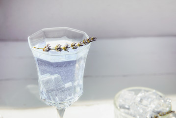 Close up Fresh lavender lemonade with flowers and ice cubes in beautiful glass on white wooden table. Detox water. Summer drink. Diet cocktail. Selective focus. Copy space.