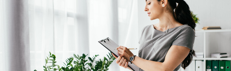 panoramic shot of pregnant woman taking notes in notebook in office