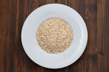 uncooked oats in white plate on wooden background