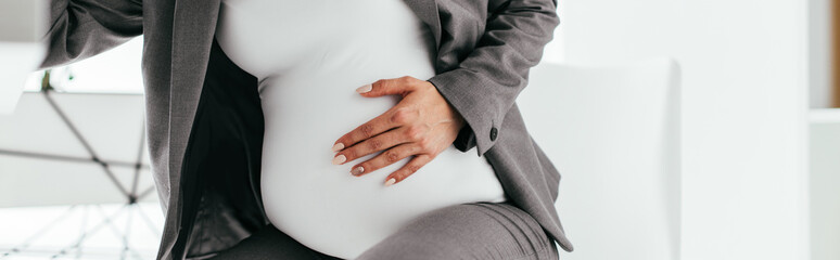 Obraz premium panoramic shot of pregnant woman holding her belly and sitting behind table